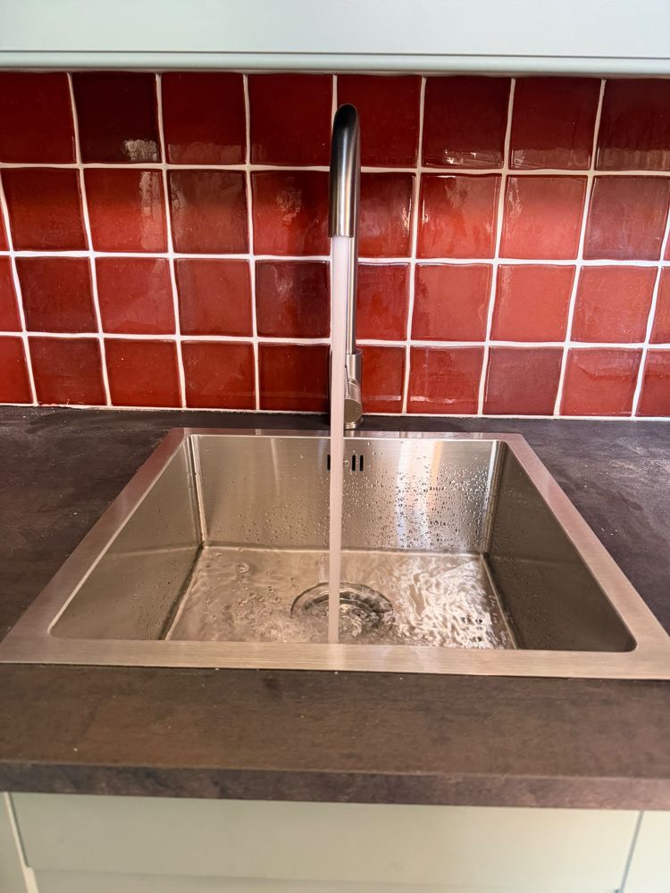 Stainless steel kitchen sink and tap fitted in front of red tiles